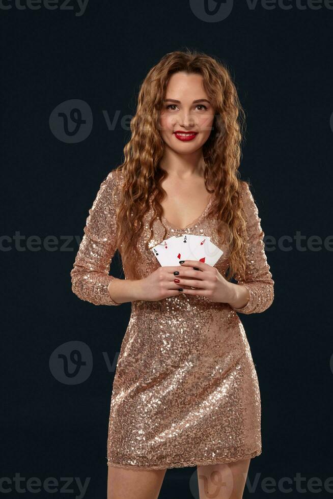 Beautiful young emotional woman in cocktail dress showing her cards to opponent, four of aces, best hand. Blcak background, studio shot photo