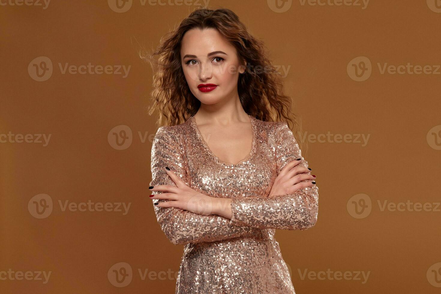 Portrait of young caucasian female in golden cocktail dress looking into the camera on brown background photo