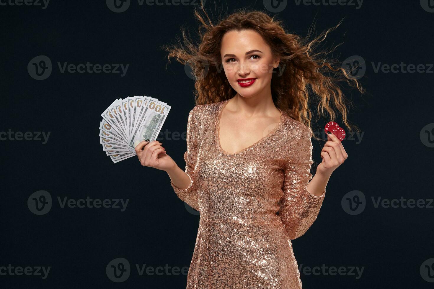 Image of lucky happy woman with brown long hair with fan of 100 dollar bills, lots of cash money, over black background photo