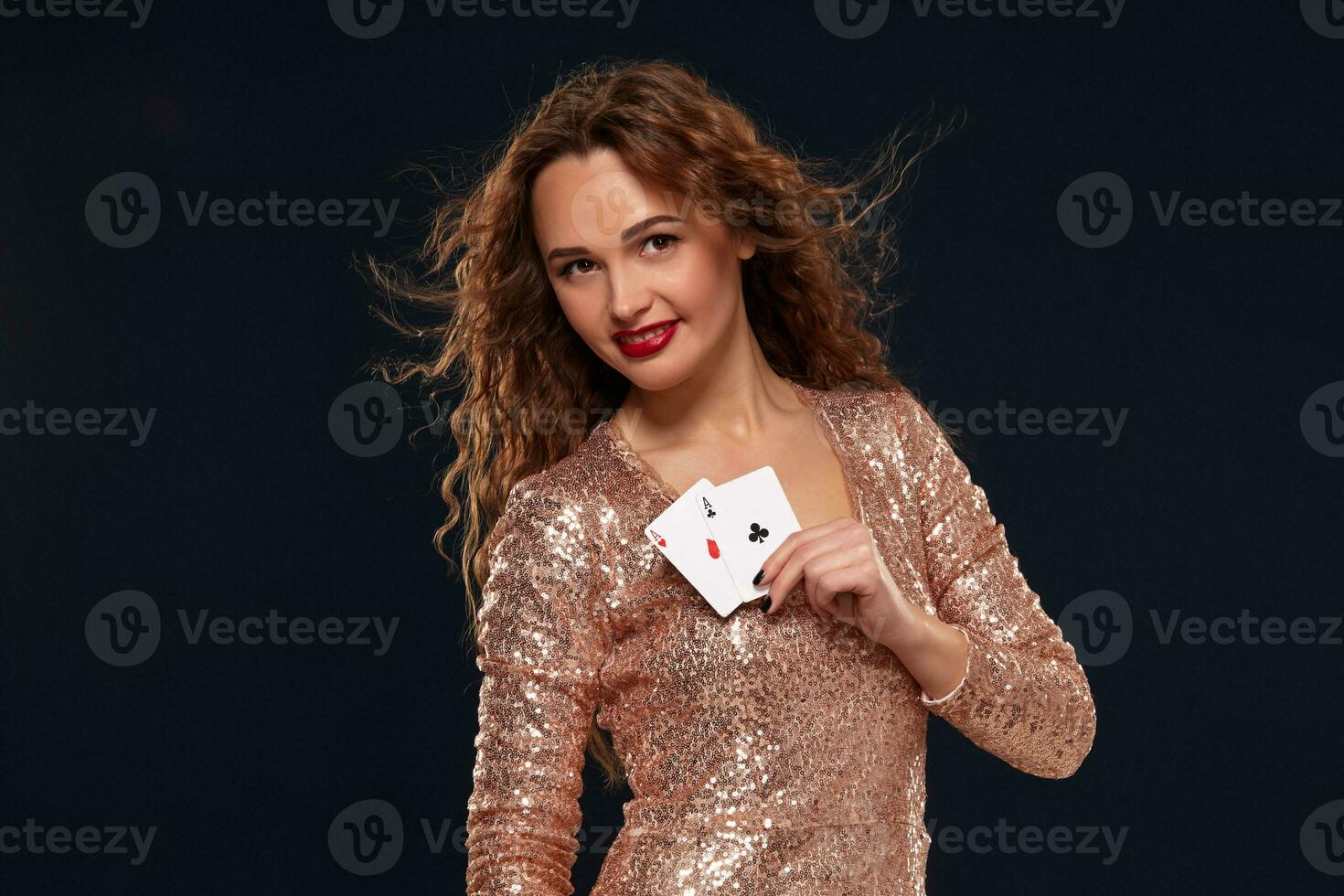 Pretty young brown-haired woman in golden cocktail dress holding pair of aces and smiling photo