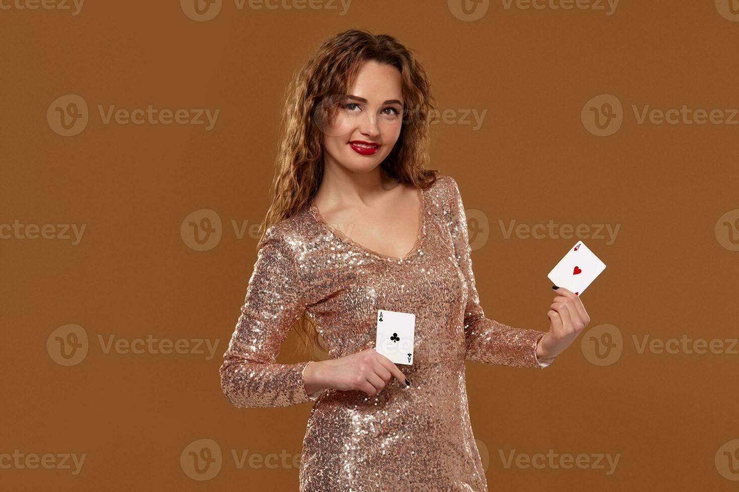 Blond woman weared in a gold glittered dress is holding two playing cards in her hands. Casino. photo