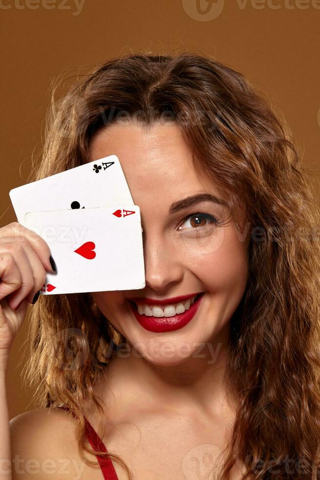 Pretty young brown-haired woman in red cocktail dress holding pair of aces and smiling photo