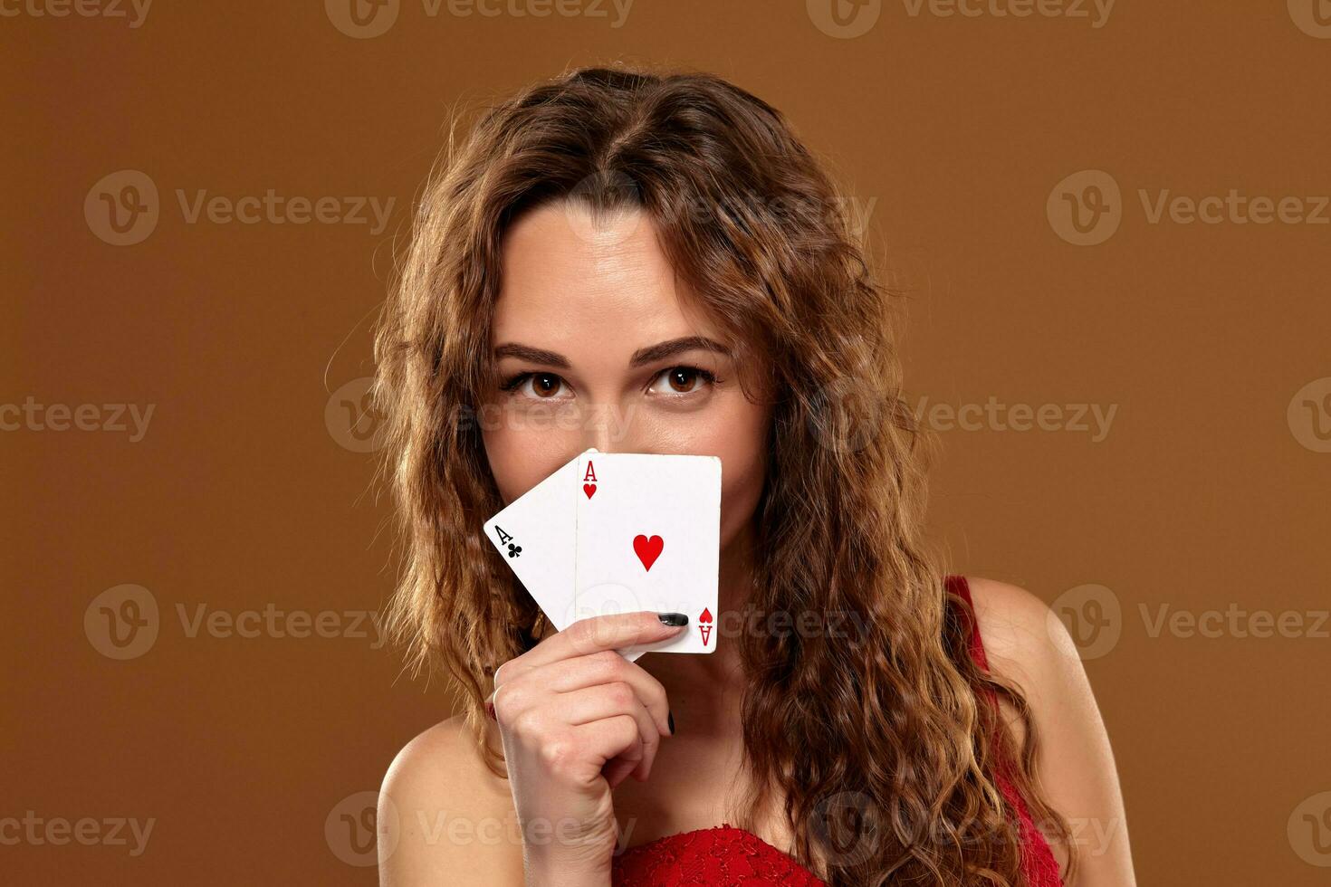 Pretty young brown-haired woman in red cocktail dress holding pair of aces and smiling photo