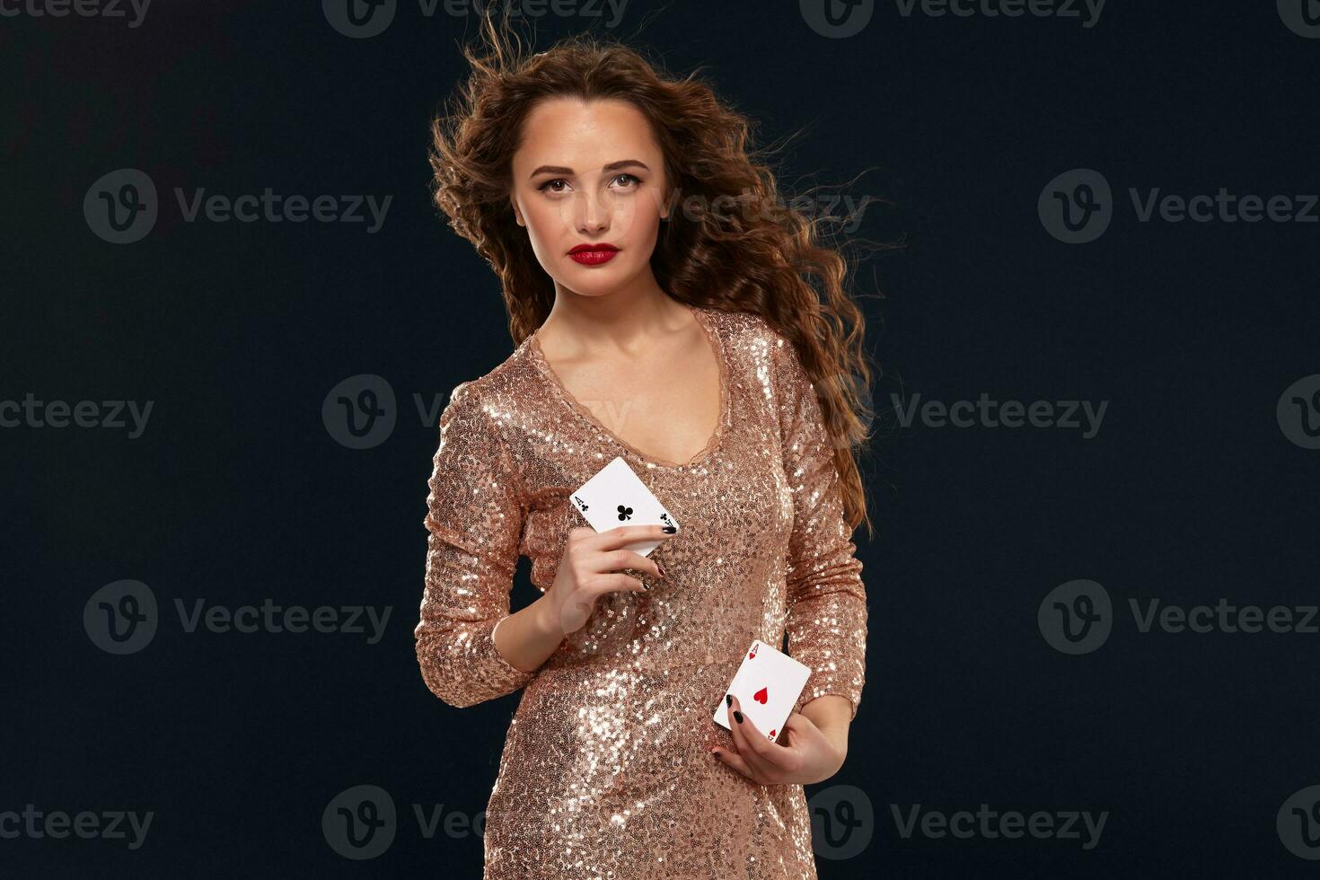 Pretty young brown-haired woman in golden cocktail dress holding pair of aces and smiling photo