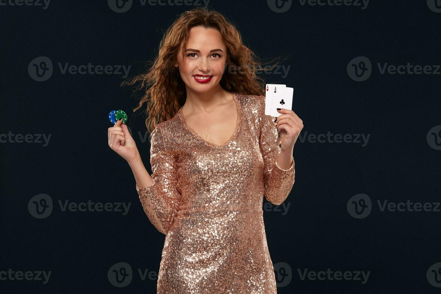 Brown-haired attractive caucasian young woman in golden cocktail dress at casino holds pair of aces and chips in her hands photo