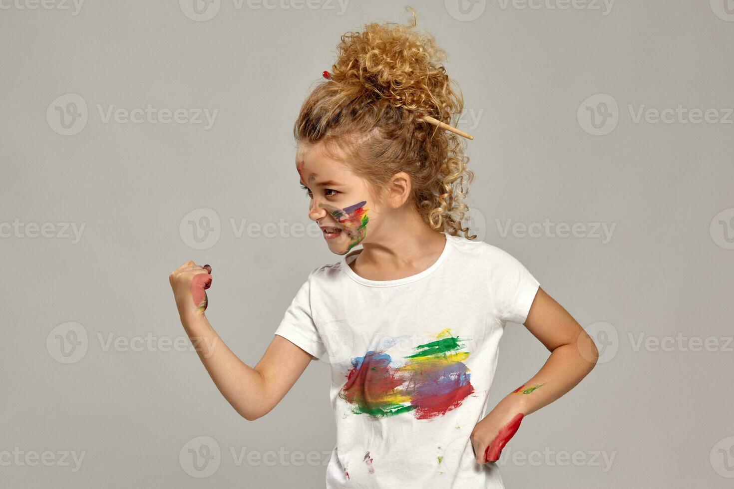 Beautiful little girl with a painted hands and cheeks is posing on a gray background. photo