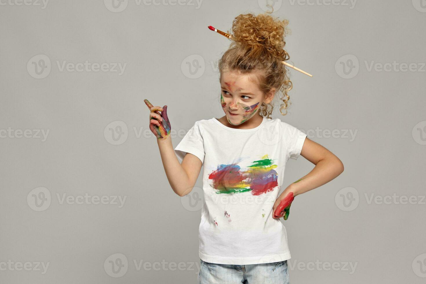 Beautiful little girl with a painted hands and cheeks is posing on a gray background. photo