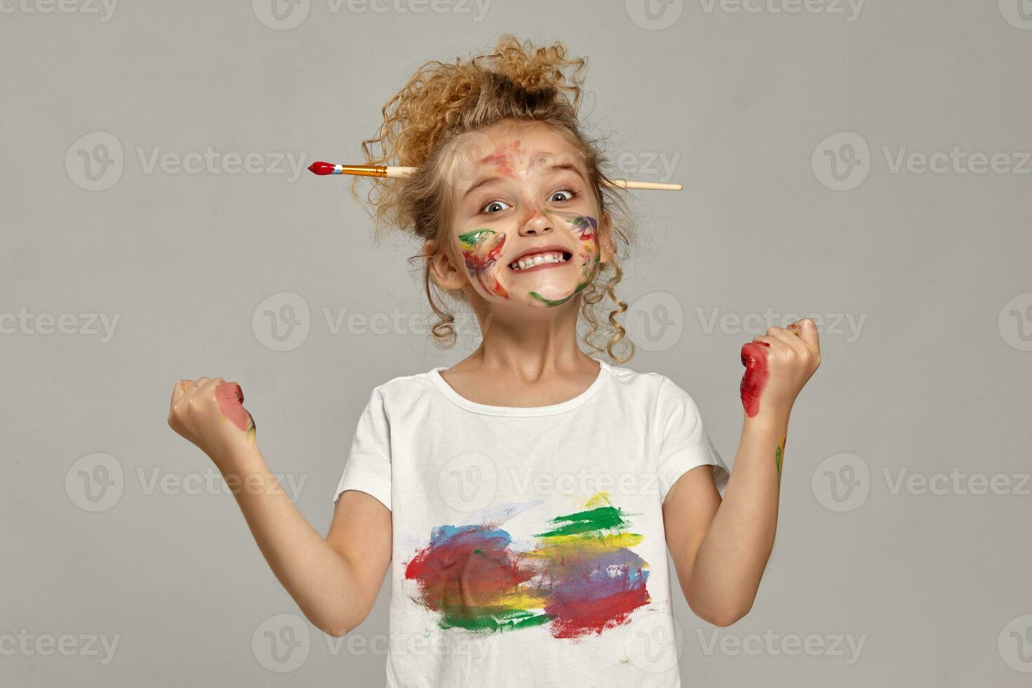 hermosa pequeño niña con un pintado manos y las mejillas es posando en un gris antecedentes. foto