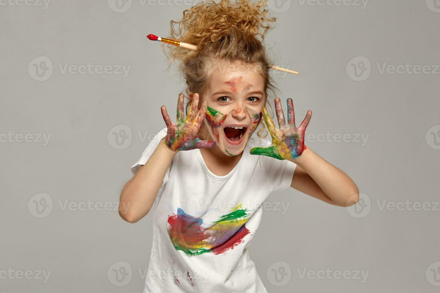 Beautiful little girl with a painted hands and cheeks is posing on a gray background. photo