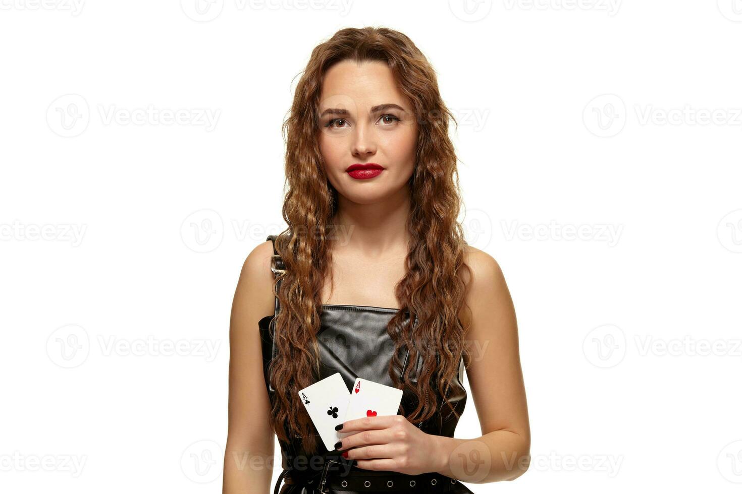 Pretty young redhead or brown-haired woman holding pair of aces in black leather dress isolated on white photo