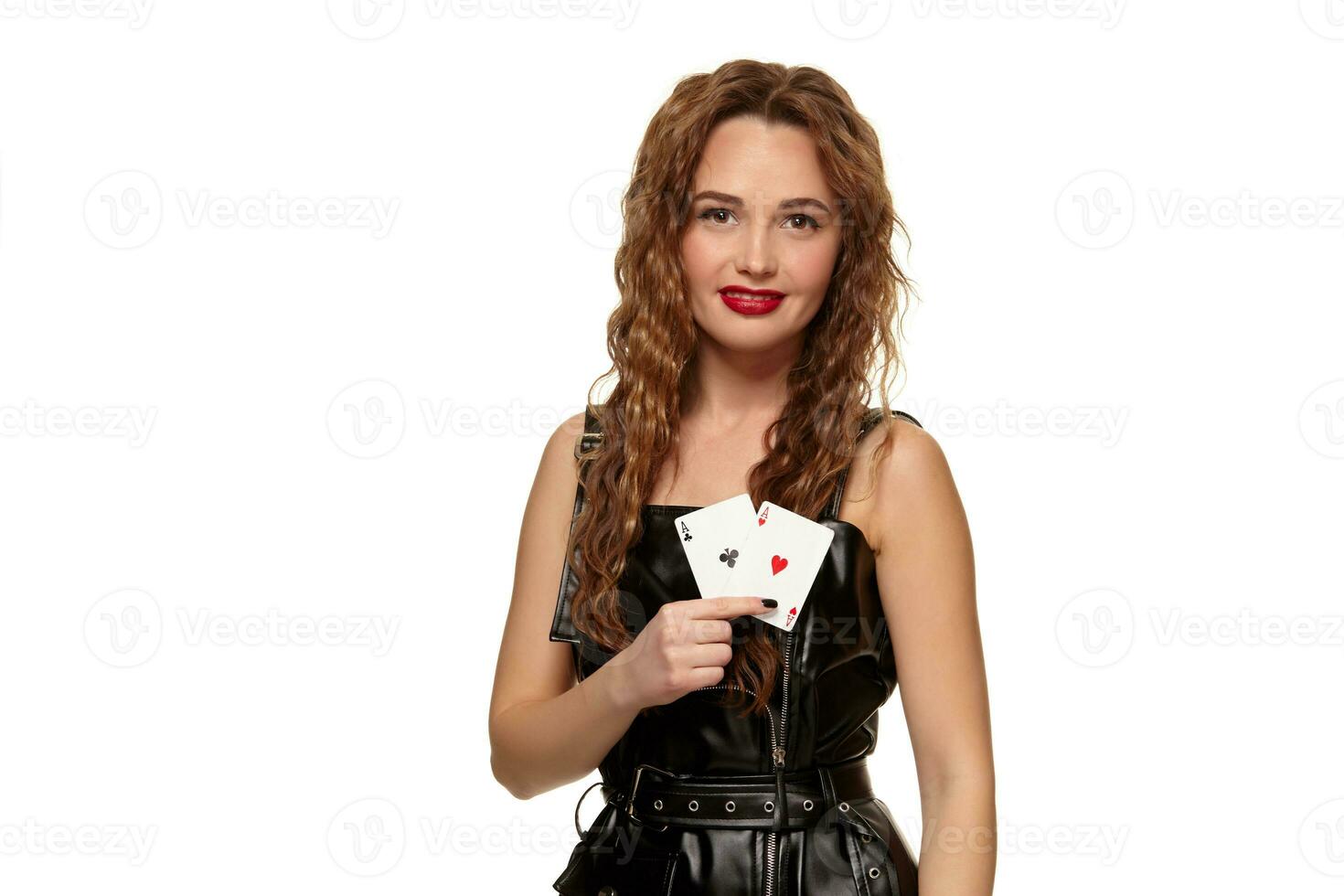 Pretty young redhead or brown-haired woman holding pair of aces in black leather dress isolated on white photo