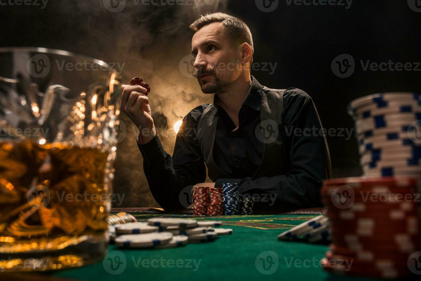 hombre es jugando póker con un cigarro y un whisky. un hombre victorioso todas el papas fritas en el mesa con grueso cigarrillo fumar. foto