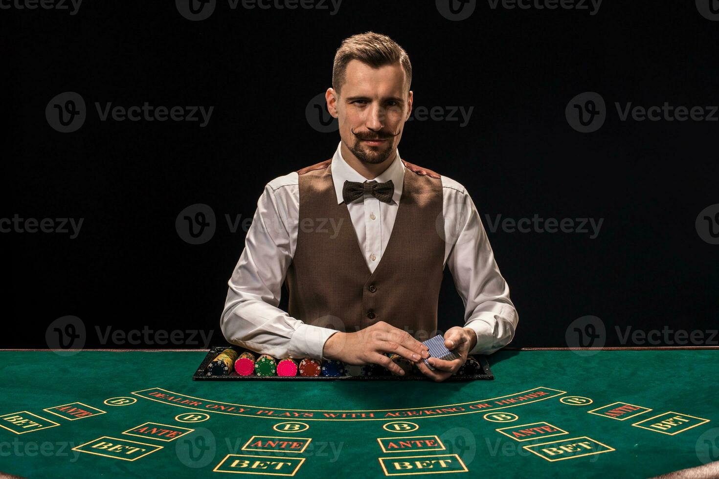 retrato de un crupier es participación jugando tarjetas, juego papas fritas en mesa. negro antecedentes foto