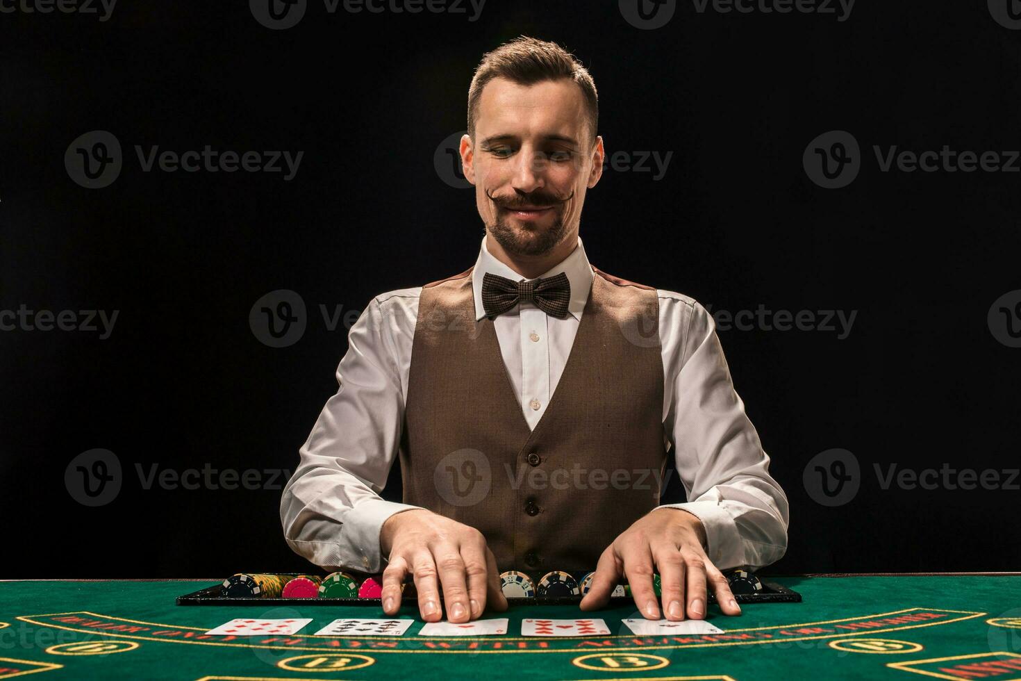 Portrait of a croupier is holding playing cards, gambling chips on table. Black background photo