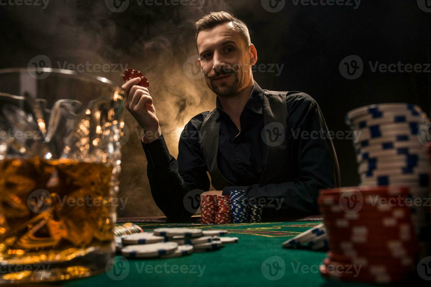 hombre es jugando póker con un cigarro y un whisky. un hombre victorioso todas el papas fritas en el mesa con grueso cigarrillo fumar. foto