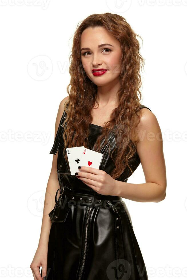 Pretty young redhead or brown-haired woman holding pair of aces in black leather dress isolated on white photo