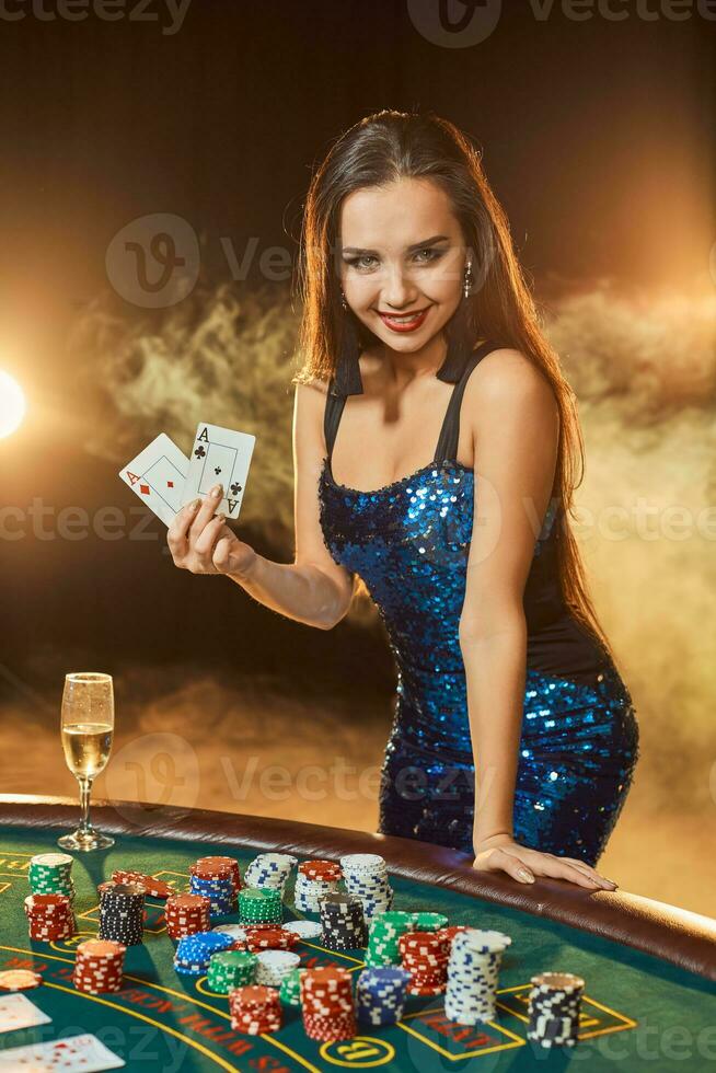 joven hermosa mujer poses cerca póker mesa en lujo casino. pasión, tarjetas, papas fritas, alcohol, dado, juego, casino - eso es como hembra entretenimiento. fumar antecedentes. foto