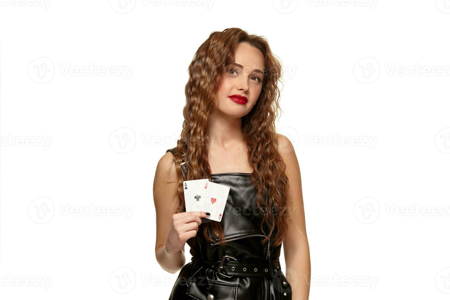 Pretty young redhead or brown-haired woman holding pair of aces in black leather dress isolated on white photo