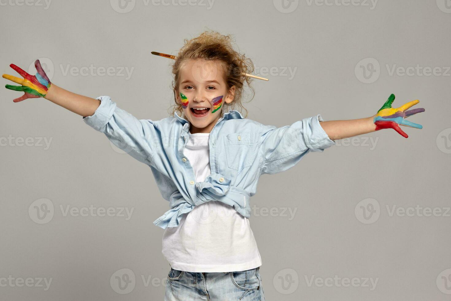 Beautiful little girl with a painted hands and cheeks is posing on a gray background. photo