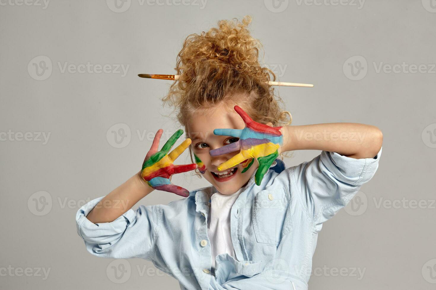 Beautiful little girl with a painted hands and cheeks is posing on a gray background. photo
