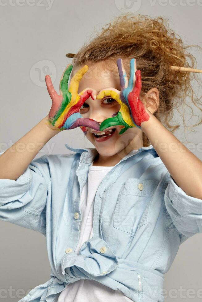 Beautiful little girl with a painted hands and cheeks is posing on a gray background. photo