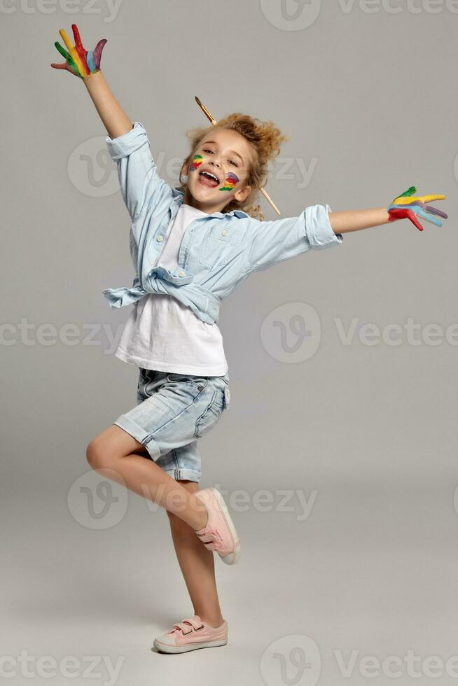 hermosa pequeño niña con un pintado manos y las mejillas es posando en un gris antecedentes. foto