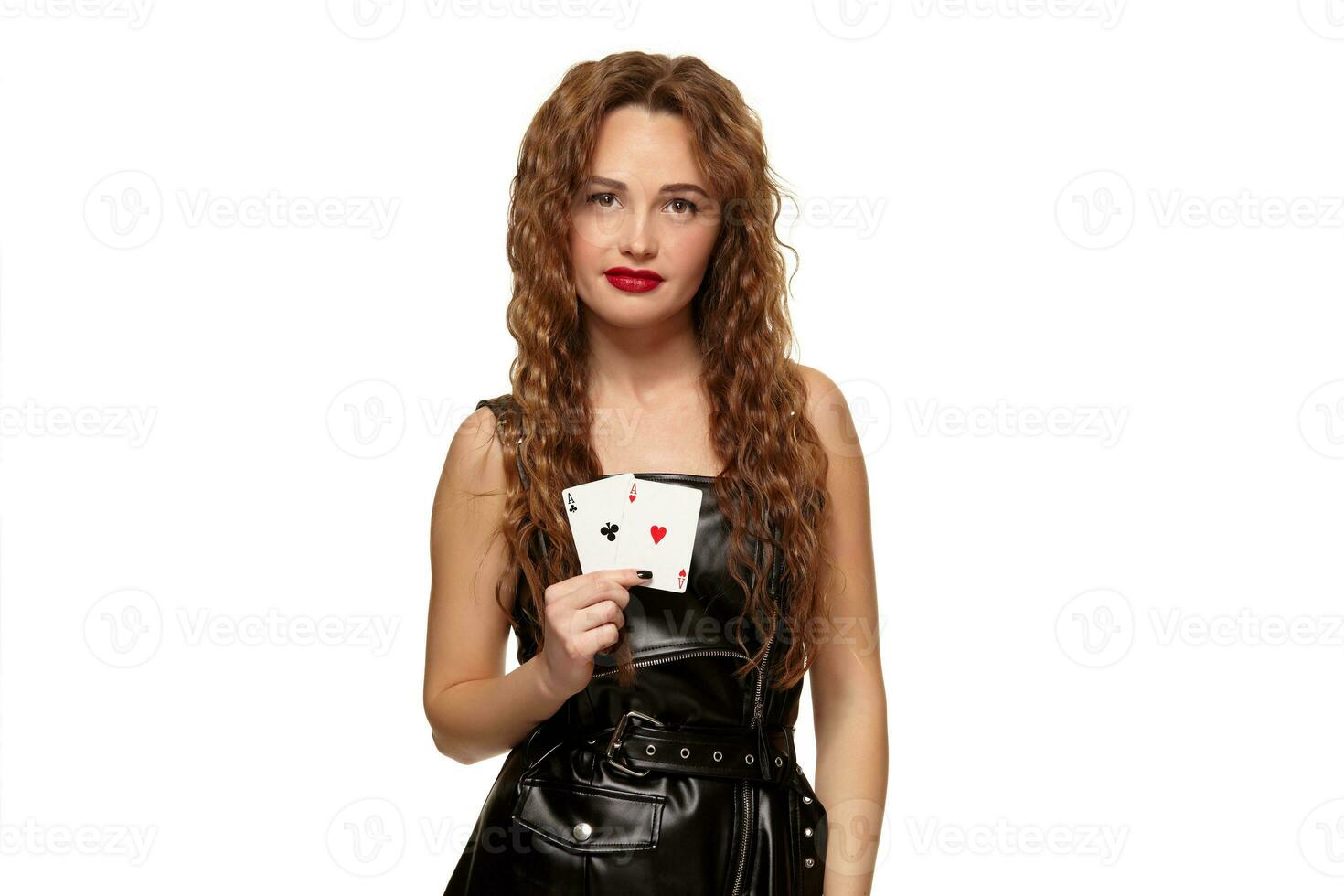 Pretty young redhead or brown-haired woman holding pair of aces in black leather dress isolated on white photo