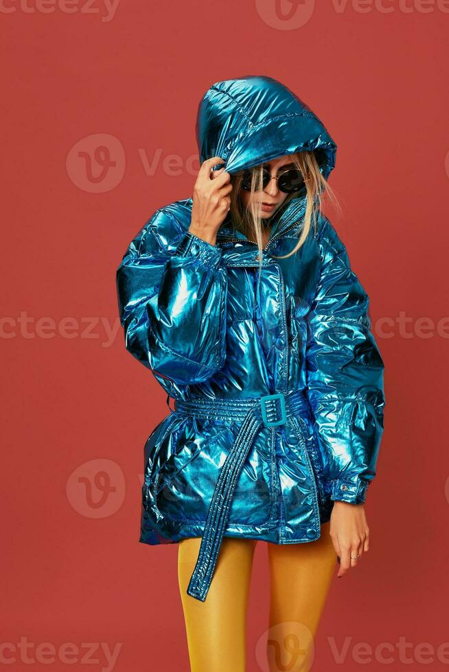 Blonde slim girl in blue down jacket covers her face from wind with hood photo