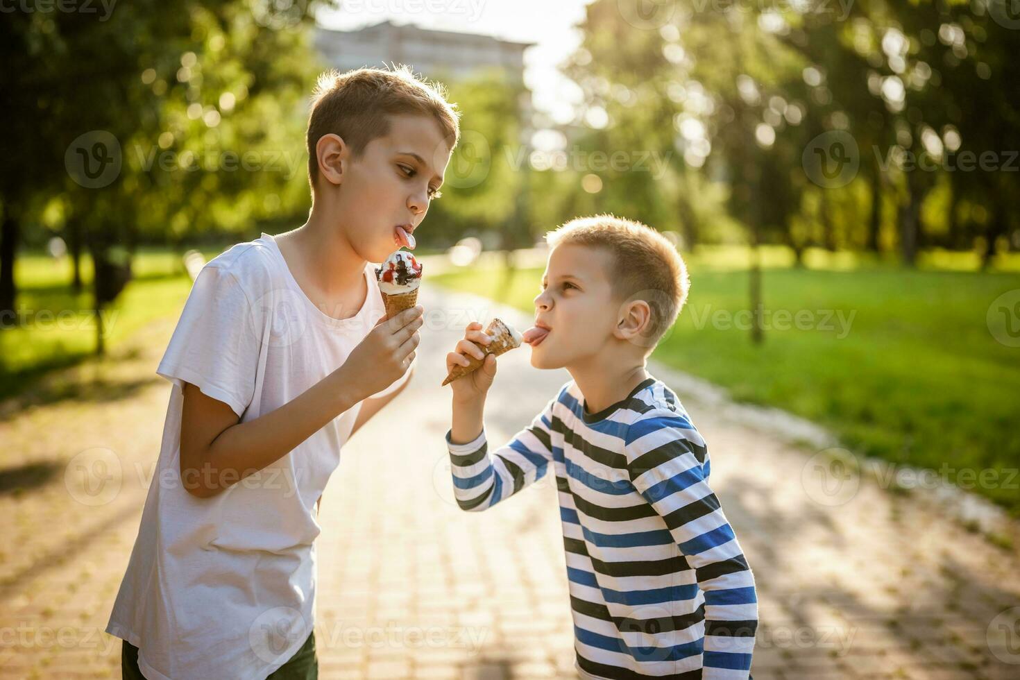 Two brothers are eating ice cream in park in summer. They are having fun and mocking at each other. photo