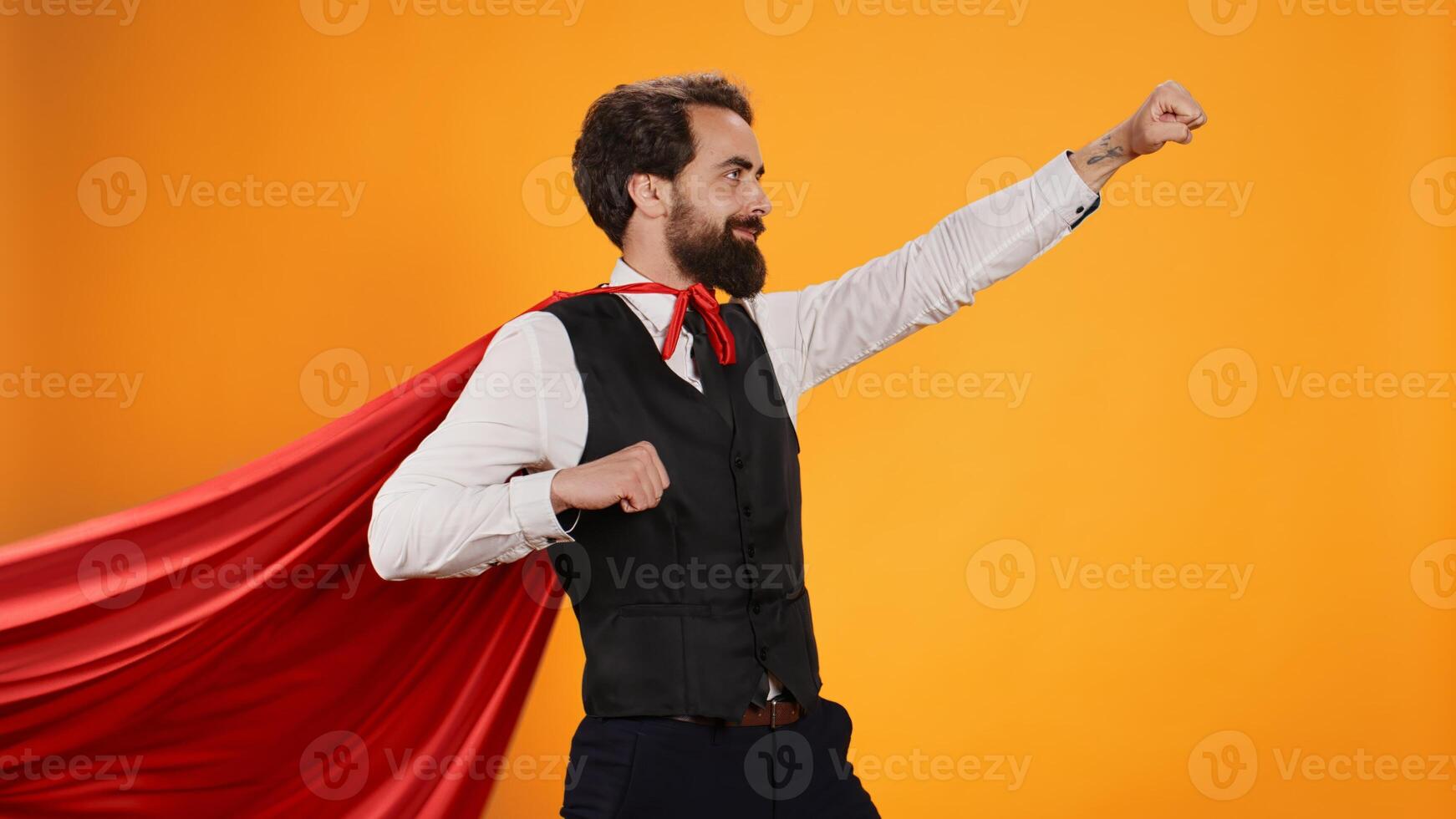 Powerful hero butler posing with red cape against yellow background, dedicated to serve consumers at fine dining restaurant. Concept of strong confident superhero character, luxury catering. photo