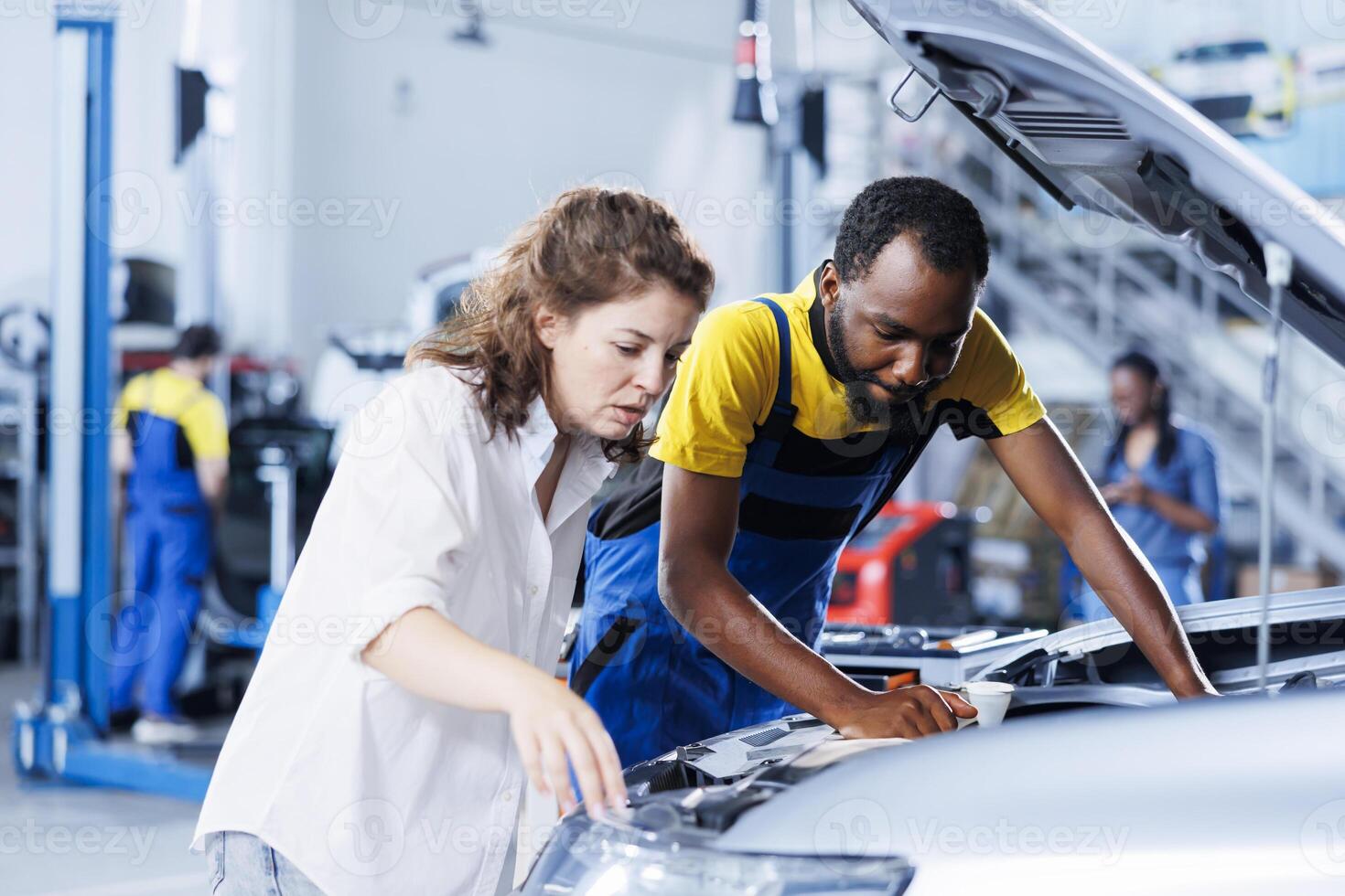 Mechanic at auto repair shop conducts annual vehicle checkup, informing customer about needed alternator replacement. Experienced garage worker talks with customer after finishing car inspection photo