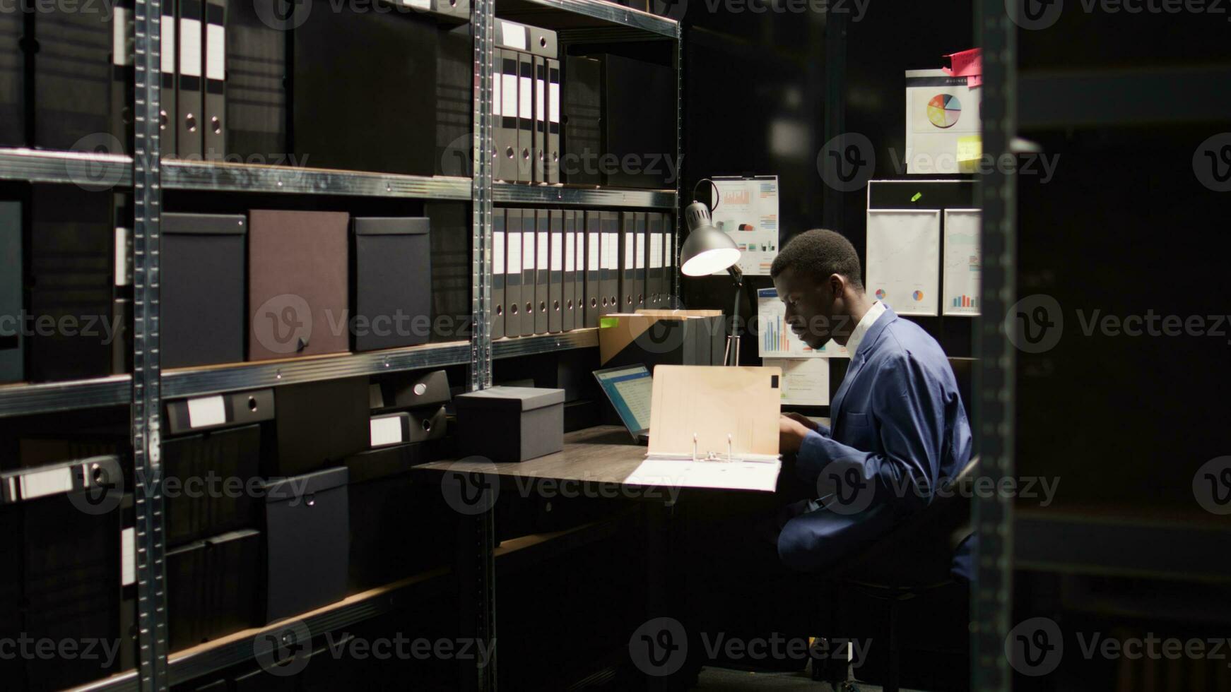 Male investigator digs deep into case, looks through evidence and skillfully analyzing data. African american law enforcement official standing to gather crime records from shelves for further study. photo