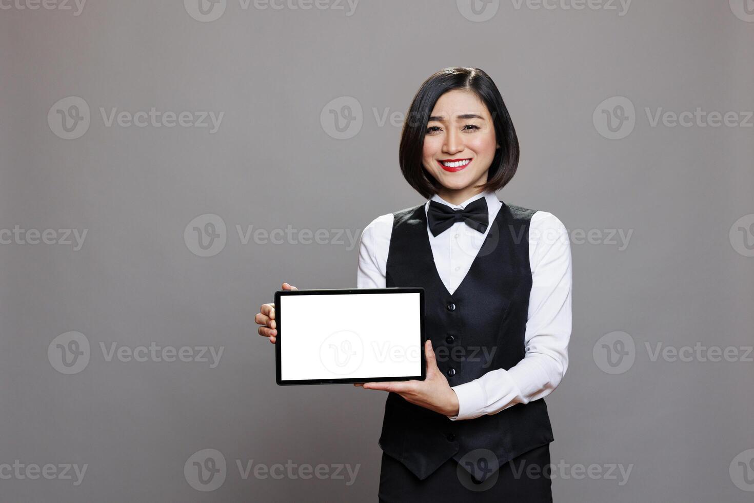 Smiling asian woman waitress showing digital tablet empty screen for catering service software app promo and looking at camera. Happy receptionist presenting blank touchscreen portrait photo
