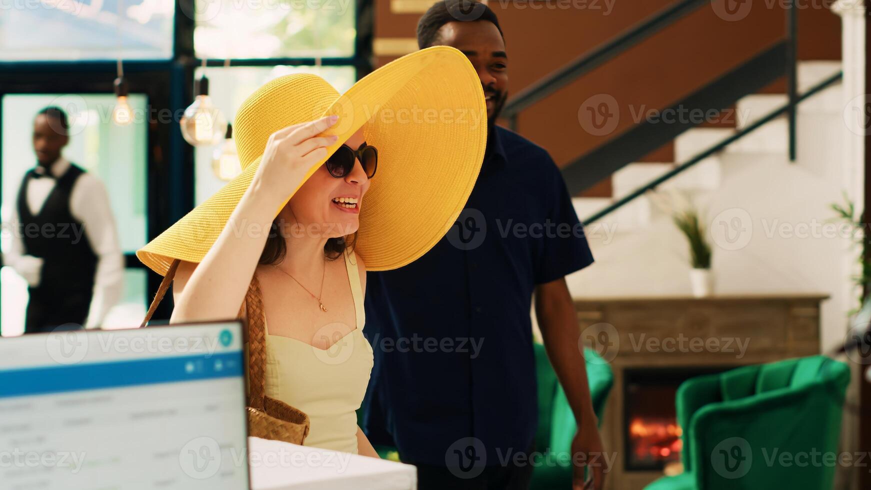 Diverse couple entering lobby at tropical summertime resort, waiting to do registration process. Guests arriving at exotic hotel counter, having room reservation accommodation. Handheld shot. photo