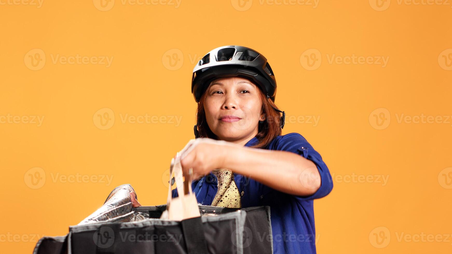 Close up shot of takeaway delivery worker preparing food order while waiting for client to answer door. Courier isolated over studio background taking meal bag out of professional thermic backpack photo