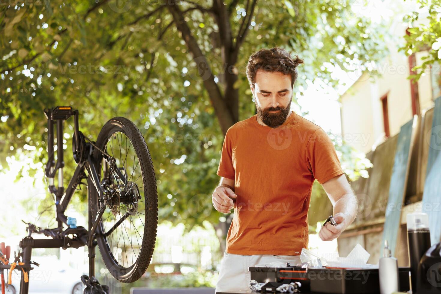 Dedicated fit and active man outside demonstrating commitment to changing and securing bicycle components for summer cycling leisure. Picture of young caucasian male arranging professional equipment photo