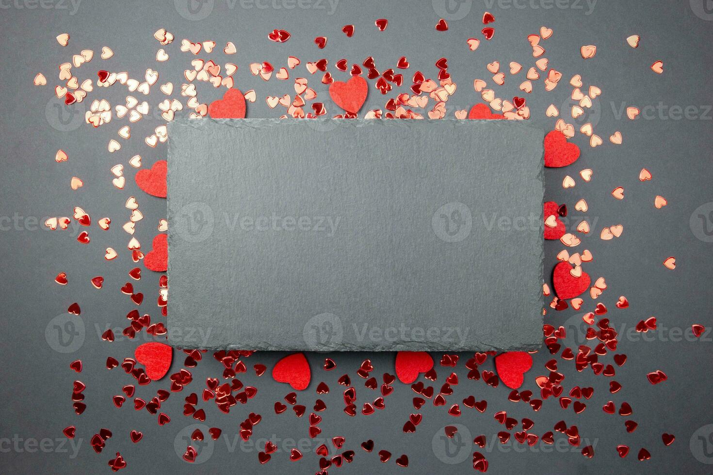 Red hearts confetti and black slate chalkboard mockup on dark background. Valentines, mothers, womens day, 8 march, birhday or wedding flat lay concept. Top view with copy space for your design. photo