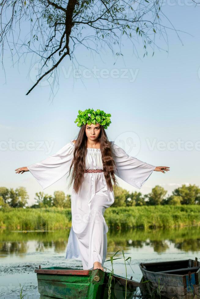 Young woman with flower wreath on her head, relaxing on boat on river at sunset. Concept of female beauty, rest in the village photo