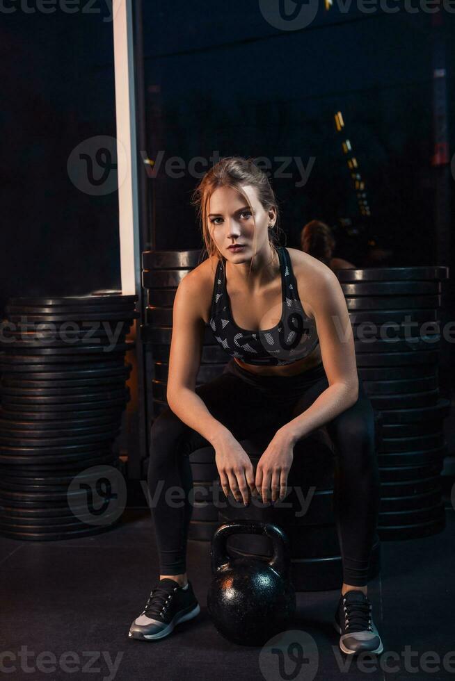 atractivo joven atleta con muscular cuerpo hacer ejercicio crossfit mujer en ropa de deporte haciendo crossfit rutina de ejercicio con tetera campana a el gimnasio foto