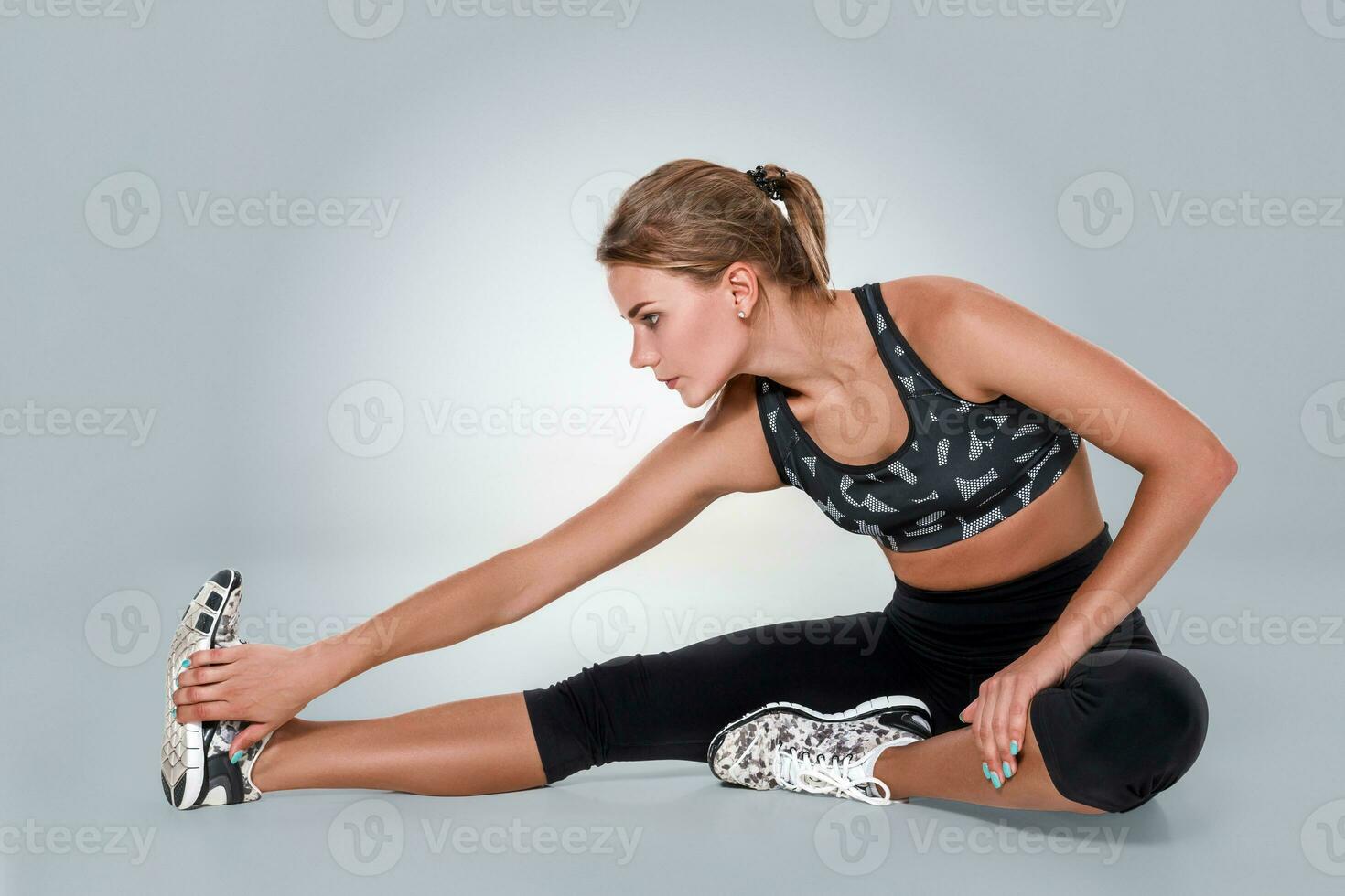 Stretching workout posture by a woman on studio gray background photo