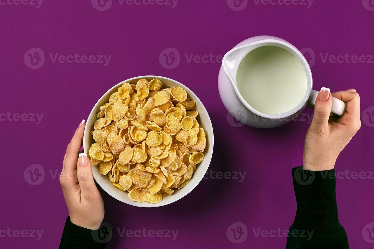 Food and people concept - hands of woman eating cereals corn flakes for breakfast and pouring milk photo