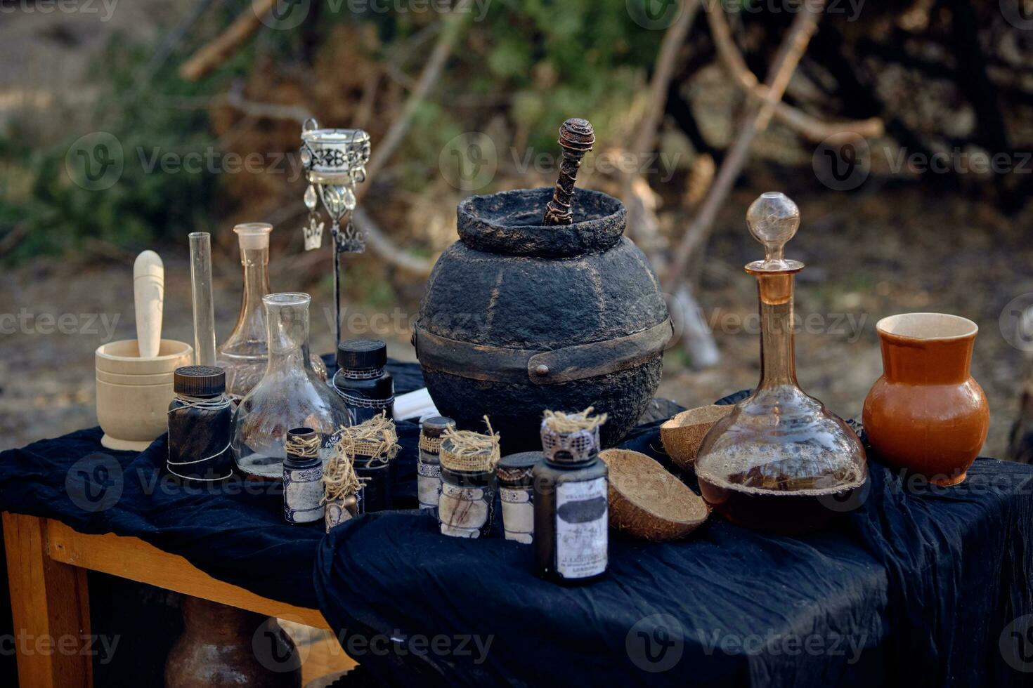 Table with accessories for spells and witchcraft standing in pine forest. Magic potion is brewed in black pot. Close-up. photo