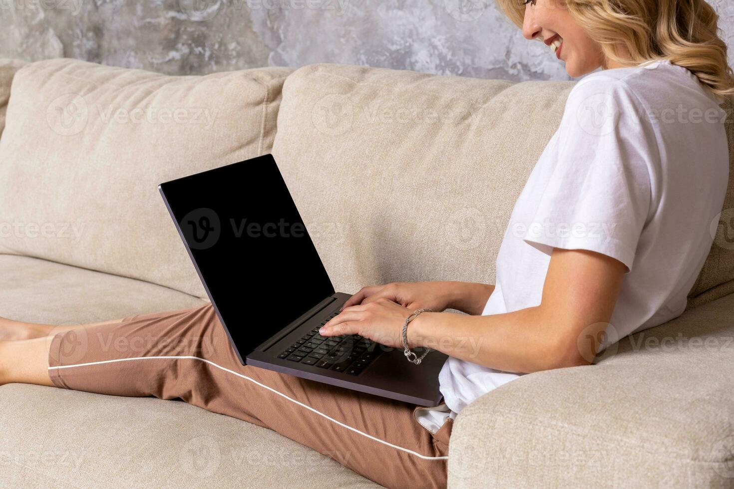 Woman on sofa working on laptop with mockup blank screen. Empty copy space on monitor for advertisement. Black screen. photo