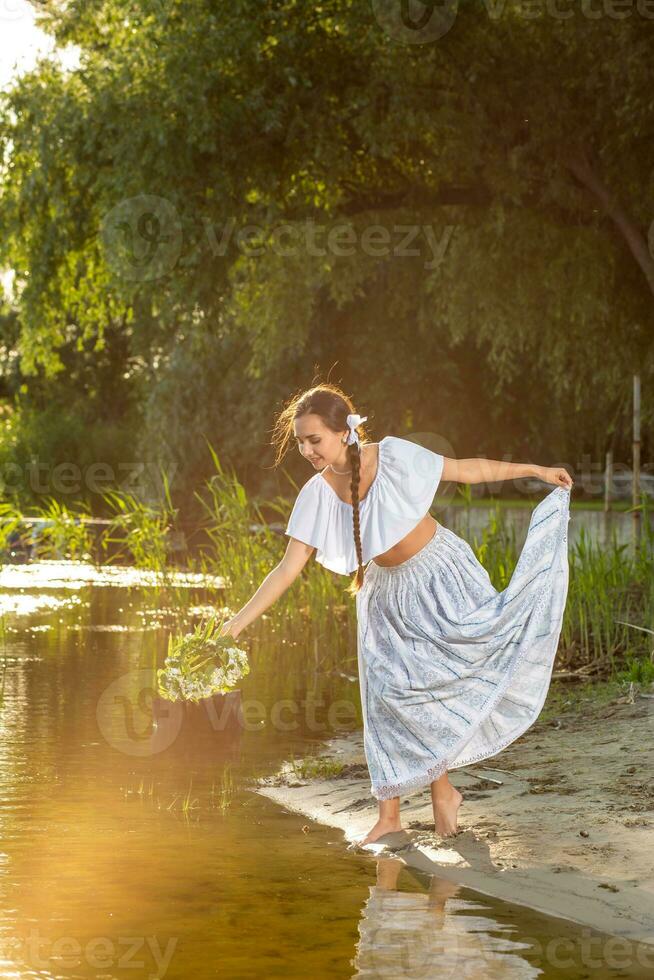 Young beautiful caucasian woman standing at the bank of river. Traditional countryside picture with girl at foreground and copy space. Sun flare photo