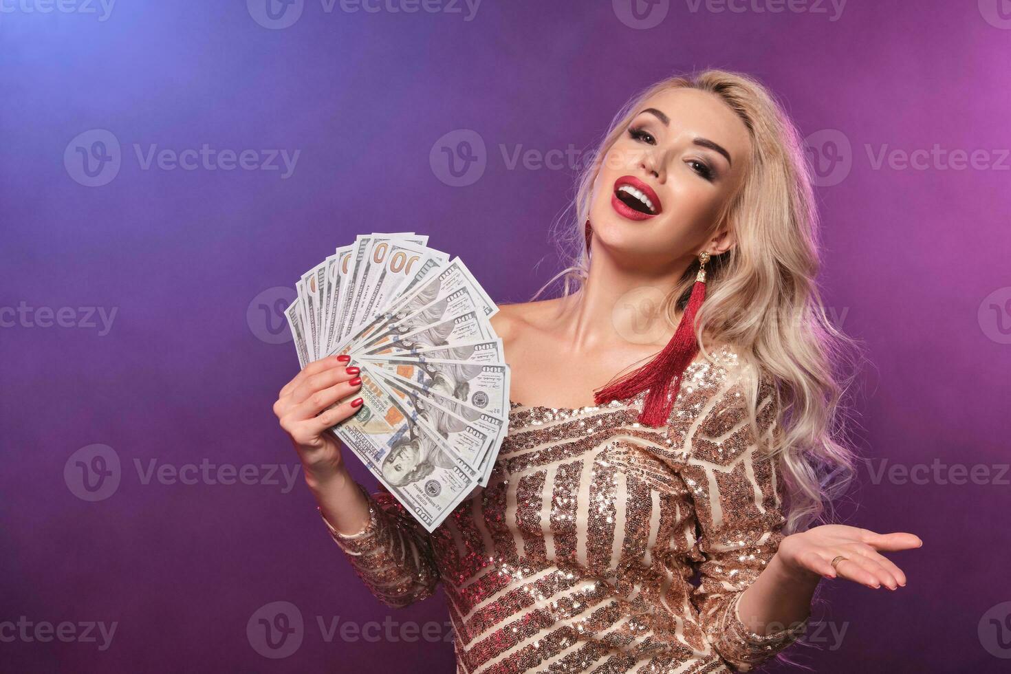 Blonde woman with a perfect hairstyle and bright make-up is posing with fan of hundred dollar bills in her hands. Casino, poker. photo
