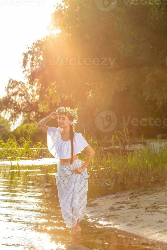 Young beautiful caucasian woman standing at the bank of river. Traditional countryside picture with girl at foreground and copy space. Sun flare photo