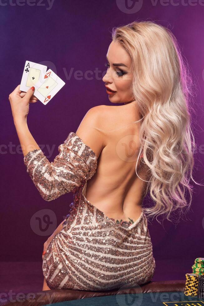 Blonde woman with a perfect hairstyle and bright make-up is posing with playing cards in her hands. Casino, poker. photo