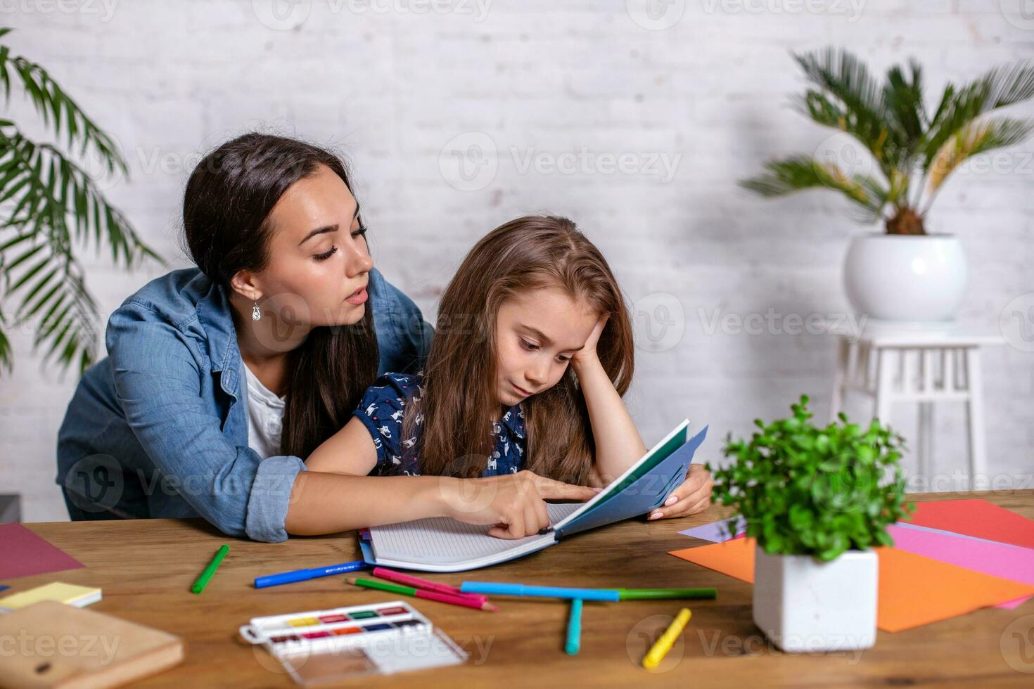 madre convirtiéndose frustrado con hija mientras que haciendo deberes sentado a el mesa a hogar en aprendizaje dificultades tarea. foto