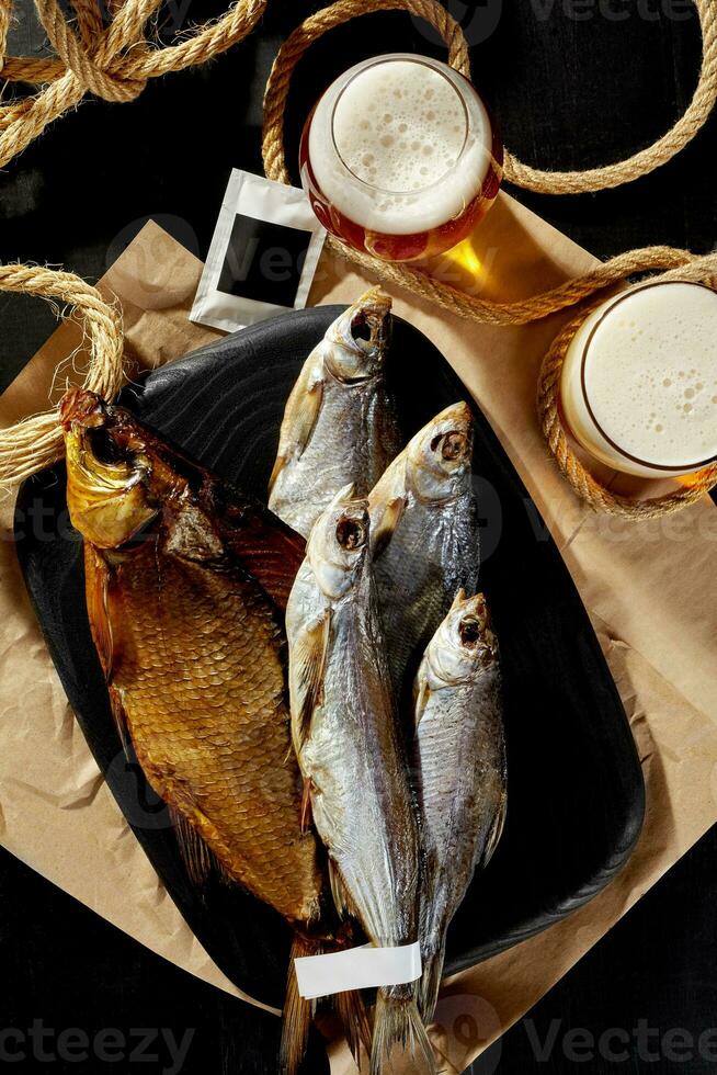 Smoked gutted bream, salted dried roach and sabrefish on wooden board with foamy light beer photo