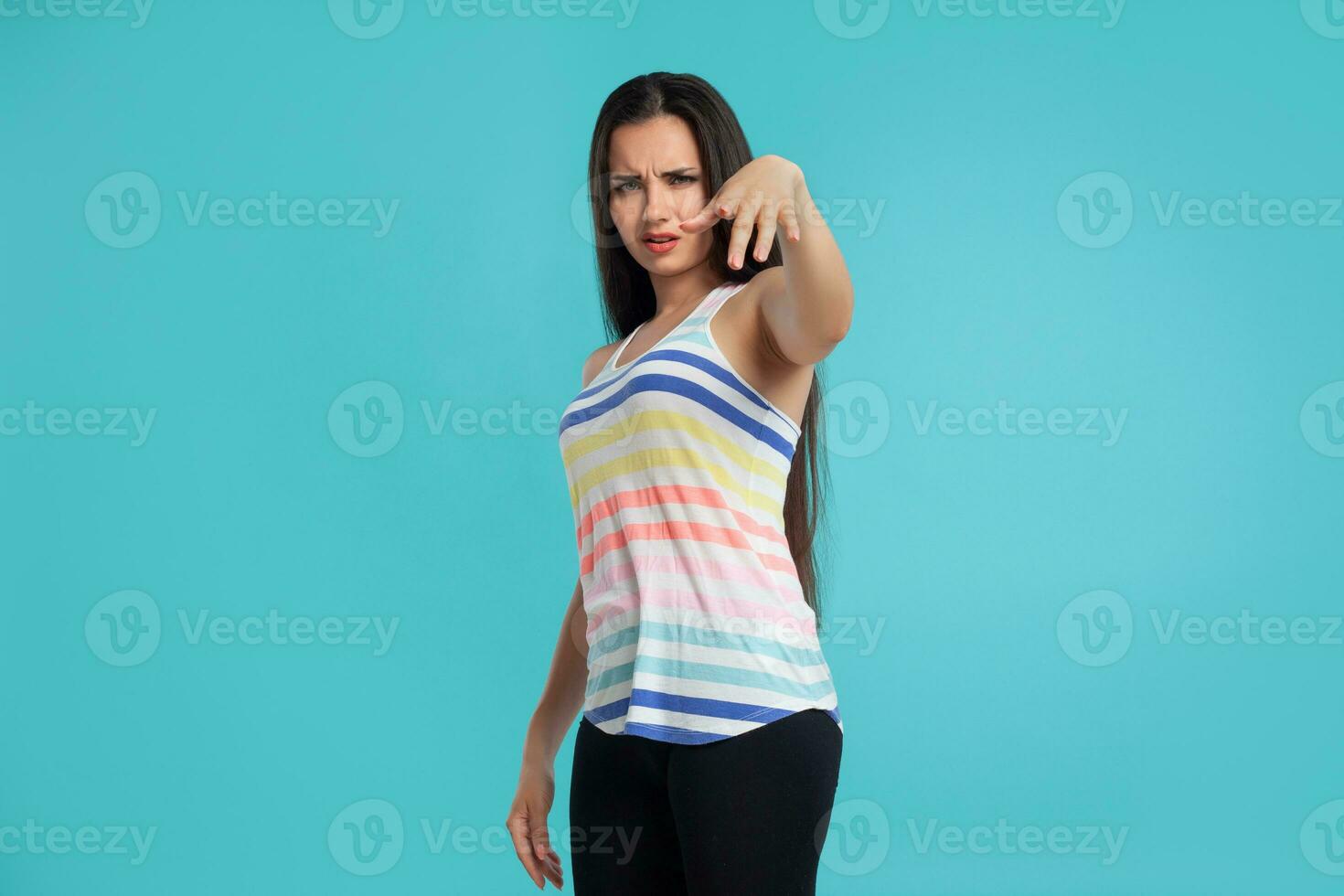 Brunette woman with long hair, dressed in striped shirt and black leggings, posing against blue studio background. Sincere emotions. Close-up. photo